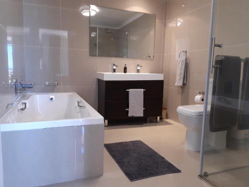 a bathroom with a tub and a sink and a toilet at 2WhiteWaters Bloubergstrand Homestay in Bloubergstrand