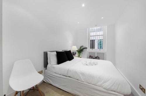 a white bedroom with a white bed and a white chair at Stunning Kensington apartment in London