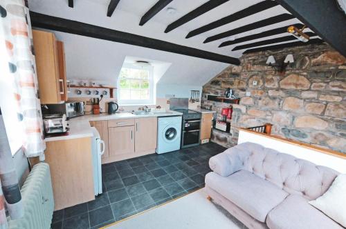 a living room with a couch and a kitchen with a stone wall at Cosy cottage for 2, sea views, large grounds. WiFi in Newport Pembrokeshire