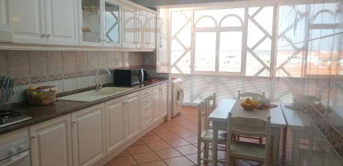 una cucina con mobili bianchi, un tavolo e una finestra di AREAL a Praia da Vagueira