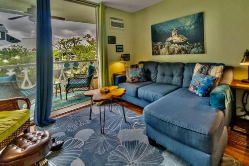 a living room with a blue couch and a large window at YOUR HAWAIIAN TROPICAL GARDEN VIEW STUDIO - KONA ISLANDER INN CONDOS condo in Kailua-Kona