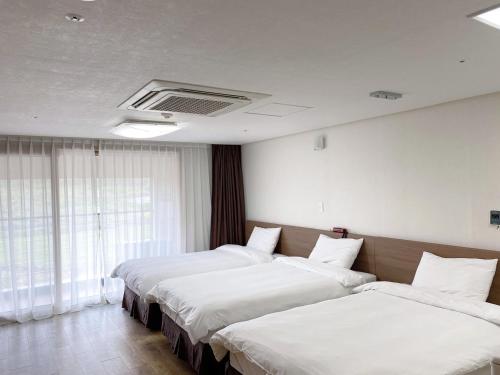 two beds in a hotel room with white sheets at Hi Jeju Hotel in Jeju