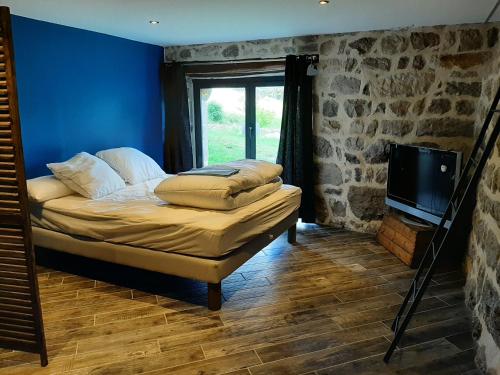 Habitación con cama, TV y pared de piedra. en Entre ruralité et modernité, en Roche