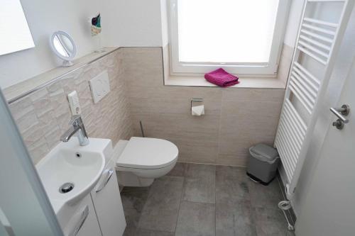 La salle de bains est pourvue de toilettes, d'un lavabo et d'une fenêtre. dans l'établissement Ferienhaus Lüttje Krabbe, à Carolinensiel