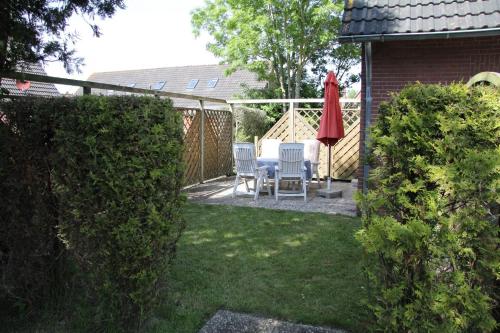 een tuin met twee stoelen en een tafel en een rode paraplu bij Ferienwohnung Skipper in Dornumersiel