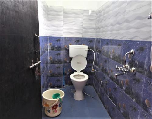 a blue tiled bathroom with a toilet and a bucket at StayApart Mount Kailash Guest House in Munsyari