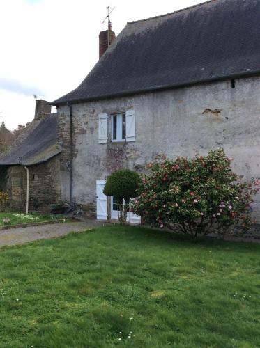 une ancienne maison en pierre avec un bush fleuri devant elle dans l'établissement Appartement dans manoir du 17eme, à Pluherlin