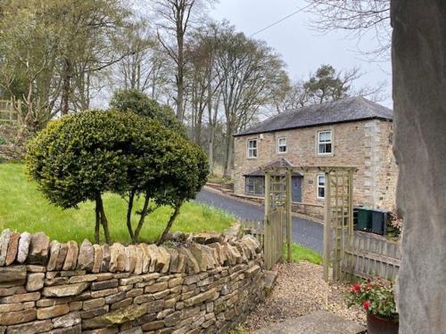 a stone wall next to a house with a tree at The Bothy at Ivy Cottage in Haltwhistle