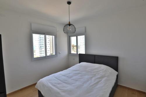 a white bedroom with a bed and two windows at דירה בטורקיז in H̱adera