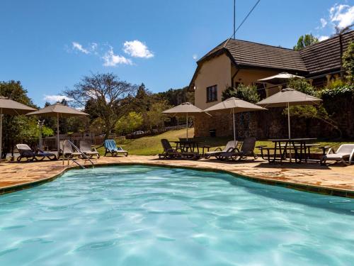 a swimming pool with chairs and umbrellas and a house at Crystal Springs Mountain Lodge in Pilgrimʼs Rest
