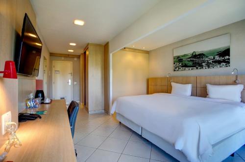 a bedroom with a large white bed and a desk at Quality Rio de Janeiro - Barra da Tijuca in Rio de Janeiro