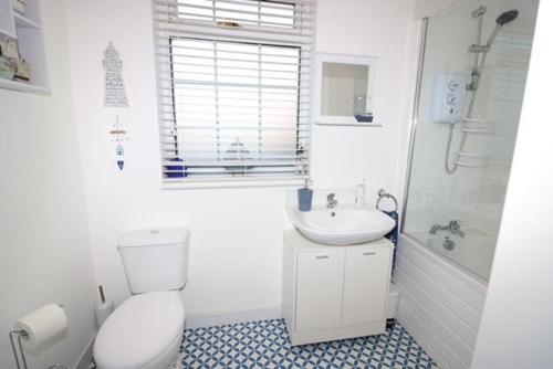 a white bathroom with a toilet and a sink at Beachcomber Cottage in Troon