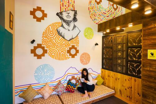 a woman sitting on a bench in a room with a mural at Zostel Manali, Vashisht in Vashisht