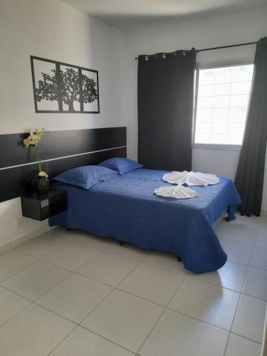 - une chambre avec un lit doté de draps bleus et une fenêtre dans l'établissement Itaguaí Flats, à Itaguaí
