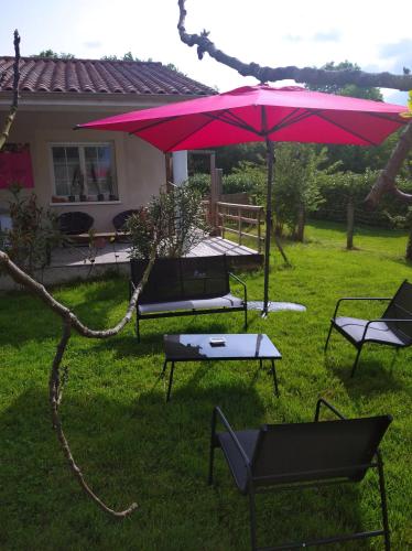 a pink umbrella and a table and chairs in a yard at Chambre d'Hôtes Les Macarons de Tata in Sainte-Eulalie