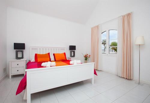 a white bedroom with a bed with colorful pillows at Villa de Carrida in Puerto del Carmen