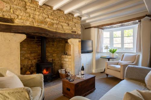 a living room with a fireplace and a stone wall at Gleneda Cottage - a renovated, traditional Cotswold cottage full of charm with fireplace and garden in Bourton on the Hill