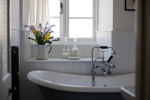 a white tub in a bathroom with flowers on a window at Gleneda Cottage - a renovated, traditional Cotswold cottage full of charm with fireplace and garden in Bourton on the Hill