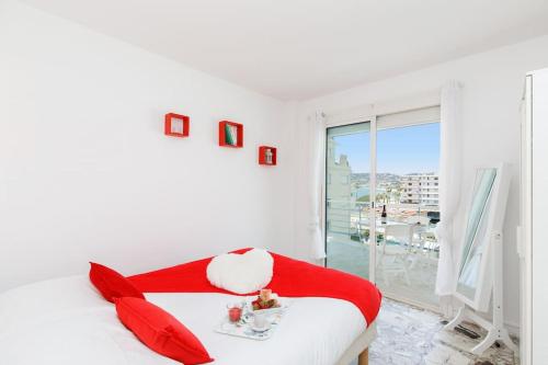 Cette chambre blanche comprend un lit avec des oreillers rouges et une fenêtre. dans l'établissement Chez Fabio YourHostHelper, à Antibes
