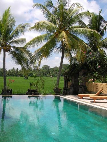 a large swimming pool with palm trees in the background at Green Field Hotel and Restaurant in Ubud