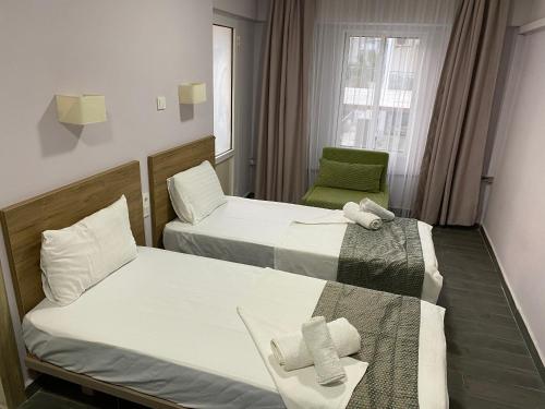 two beds in a hotel room with a green chair at Baskent Otel in Didim