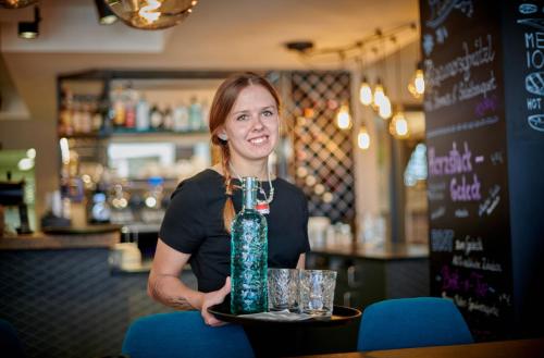a woman sitting in a bar holding a bottle at Hotel & Restaurant Herzstück Waldkirchen in Waldkirchen