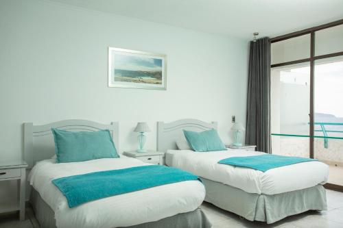 two beds with blue pillows in a white room at Hotel Rocas de Bahía in Bahia Inglesa