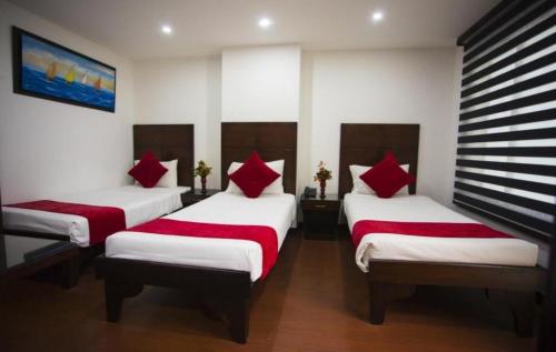 a room with three beds with red pillows at Hotel Bogotá Real DC in Bogotá