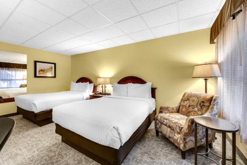 a hotel room with two beds and a chair at The Academy Hotel Colorado Springs in Colorado Springs
