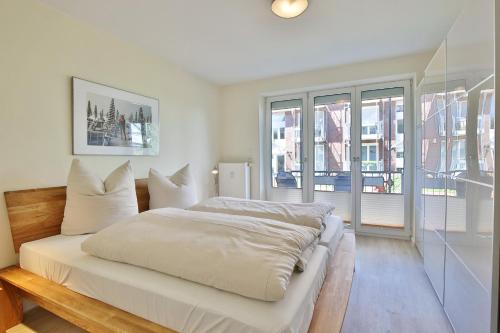 a white bedroom with a bed and windows at Strandduene Stranddüne Appartement 3 in Haffkrug