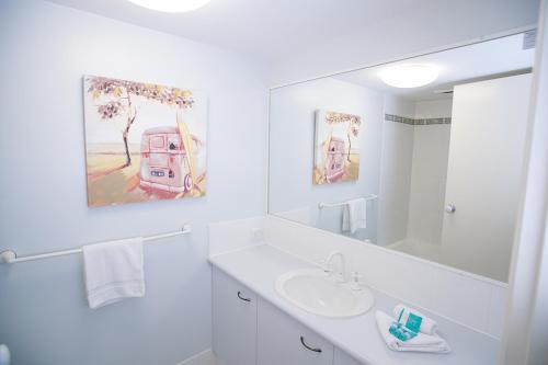 a white bathroom with a sink and a mirror at San Marino by the Sea Apartments in Marcoola