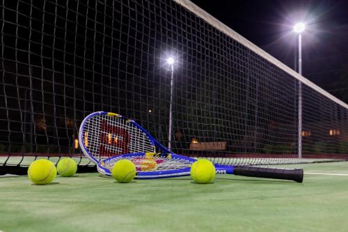 a tennis racket and balls on a tennis court at night at Sealine Beach, a Murwab Resort in Mesaieed