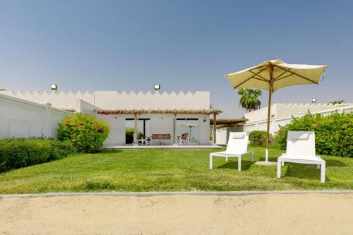 two white chairs and an umbrella in a yard at Sealine Beach, a Murwab Resort in Mesaieed