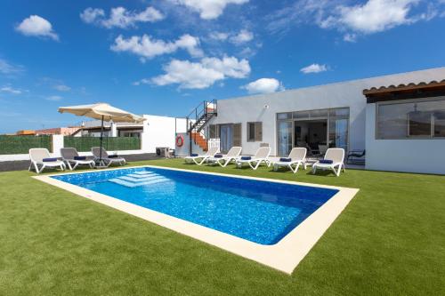 een achtertuin met een zwembad en stoelen en een huis bij Luxury Villa Perla in Caleta De Fuste