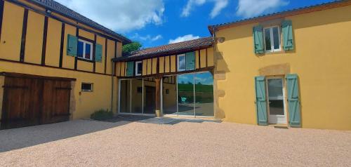 a large yellow house with glass doors in a driveway at maison d'hôtes Le Courty in Blousson-Sérian