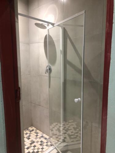 a shower with a glass door and a tile floor at Pozi Guest House in Sasolburg