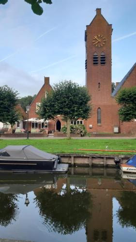 a church with a clock tower and a boat in the water at Hotel Stedswal in Sloten