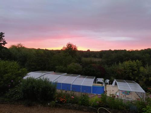 a greenhouse in a garden with the sunset in the background at Gîte La Pironnière - Piscine, Nature, au bord de la Rivière in Montreuil-sur-Maine