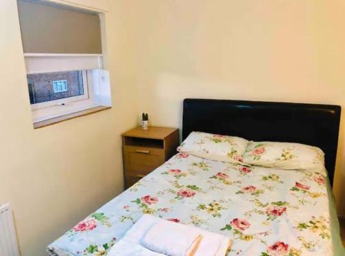 1 dormitorio con 1 cama con colcha de flores y ventana en Private room 4-5 minutes drive to Luton Airport en Luton