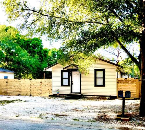a small yellow house with a fence and a tree at Two Fully Equipped Apartments and a Studio 5 miles from the beach in St. Petersburg