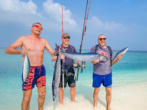three men standing on the beach holding a fish at Sabba Beach Suite , Fodhdhoo - Maldives in Velidhoo