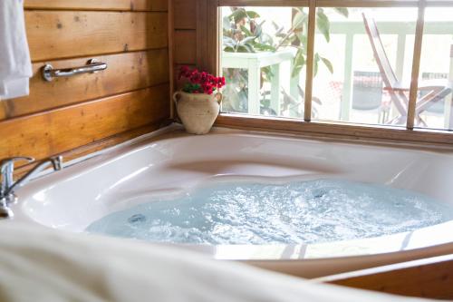 a bath tub with a window and a vase of flowers at Eden Ramot Chalets in Moshav Ramot