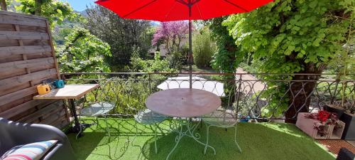 a table and chair with a red umbrella on a balcony at Le gîte du Tarn in Aguessac