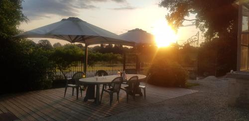 a table and chairs with an umbrella and the sun at Au p’tit bonheur d’augé in Augé