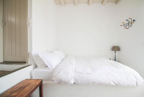 a white bed with white pillows and a wooden table at Enea by TinosHost in Tinos Town