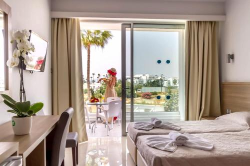a hotel room with two beds and a table with a woman on the balcony at Bellini Hotel in Ayia Napa