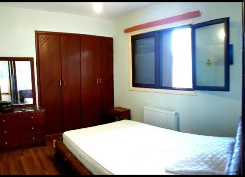 1 dormitorio con cama, ventana y armarios de madera en Palm Beach Apartment, en Oroklini