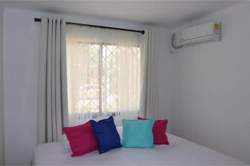 a white bed with colorful pillows in front of a window at Alojamiento espectacular, cerca al Malecón del Río, Puerta de Oro y CC Buenavista - Duchas con agua caliente in Barranquilla