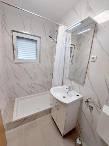 a white bathroom with a sink and a tub and a mirror at Apartmani Korljan in Gradac