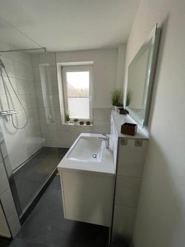 a white bathroom with a sink and a mirror at Wohnungen mit direktem Meerblick in Laboe